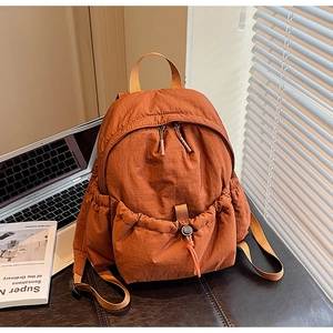 Detailed shot of caramel nylon backpack with orange drawstring on a leather bench