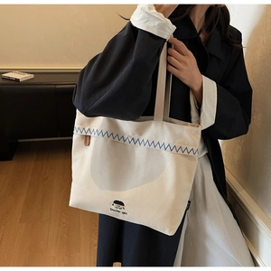Detailed shot of canvas tote bag with blue zigzag stitching and Docile-girl logo label