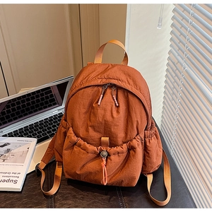 Detail view of brick orange nylon backpack with drawstring front pocket in workspace setting