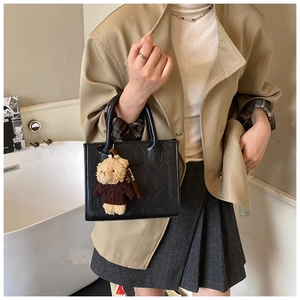 Detail of black embossed tote bag with teddy bear charm paired with a pleated skirt