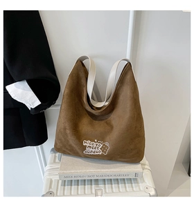 Close-up of brown suede shoulder bag with white embroidery on a striped suitcase