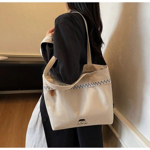 Detail of canvas tote bag showing Docile-girl branding and blue wavy stitching accent