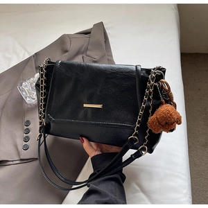 Close-up of black textured leather handbag with gold chain strap and teddy bear charm