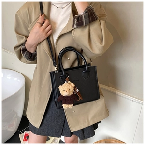 Detail of black leather crossbody square bag with cute brown bear plush pendant