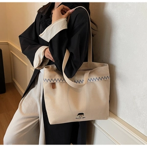 Action shot of beige canvas tote bag with blue wave embroidery and Docile girl print