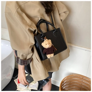 Detail of black leather crossbody bag with a cute teddy bear charm on model