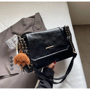 Detail of black leather underarm bag featuring gold metal bar and cute teddy bear charm