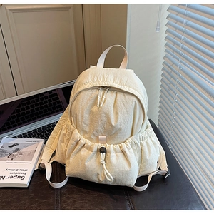 Detail of off-white nylon backpack with drawstring pocket and side buckle on leather desk