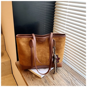 Detailed macro of brown suede tote bag with fringe charm and fashion brand plaque