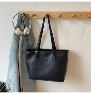 Detail of black faux leather tote bag with crinkled texture and metal buckle detail