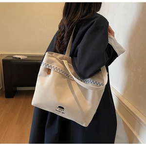 Detail view of cream canvas tote bag with blue embroidery and cartoon patch on model