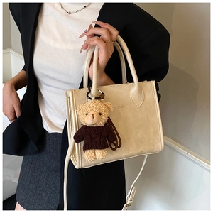 Detail view of a beige faux leather tote bag with a cute brown plush bear charm