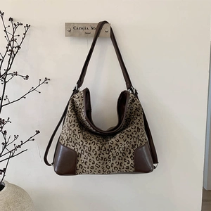 Detail of leopard print tote bag with brown leather trim hanging on a wooden hook