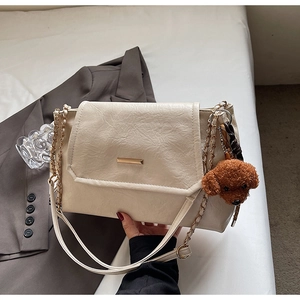 Close-up of cream PU leather handbag with gold bar detail and teddy bear charm