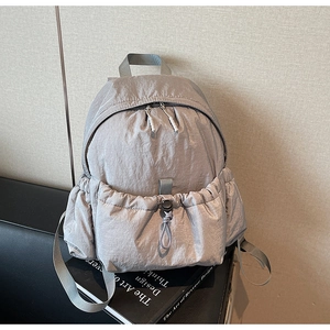 Detail view of light grey nylon backpack showing drawstring front pocket and dual zippers
