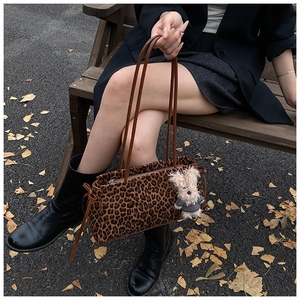 Detalle del bolso con estampado de leopardo y colgante de oso en un banco de parque