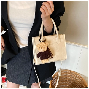 Detail of beige square handbag with brown teddy bear charm on professional model