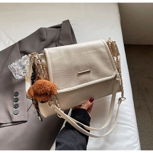 Detail of beige wrinkled leather shoulder bag with gold metal bar and teddy bear charm