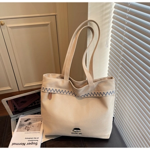 Detail of beige canvas tote bag with blue wave embroidery and Docile-girl branding