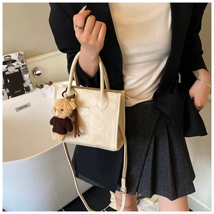 Detail of cream leather crossbody bag with HOCOMU logo and cute teddy bear charm