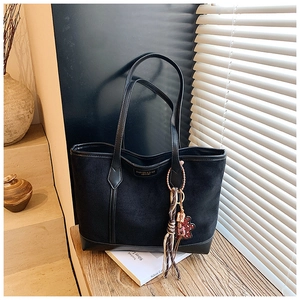 Detail view of large matte black tote bag with leather trim and woven decorative pendant