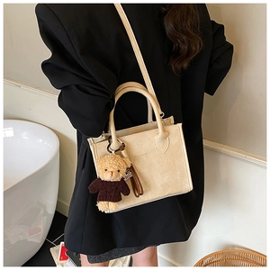 Detail view of cream vintage crossbody bag with cute teddy bear charm and sleek top handle