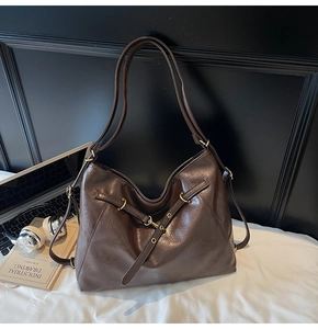 Detail of dark brown oil wax leather shoulder bag with gold rings and soft texture