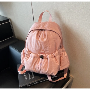 Detail of pink nylon backpack featuring a drawstring front pocket and dual zippers