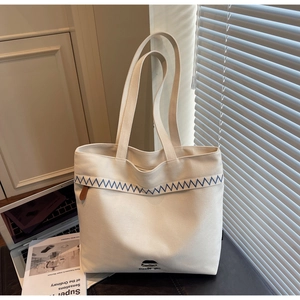 Detail of minimalist canvas tote with blue wavy embroidery and leather tag on desk