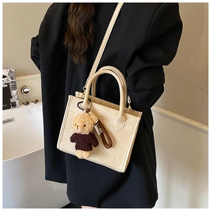 Detailed view of cream-white tote bag with a teddy bear charm on black blazer