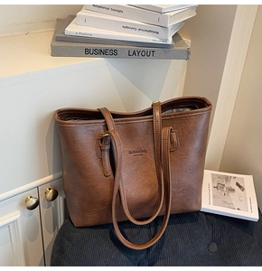 Detail of vintage brown tote bag with embossed text and dual straps on soft stool