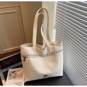 Close-up of minimalist cream canvas tote with blue wavy stitching and character graphic