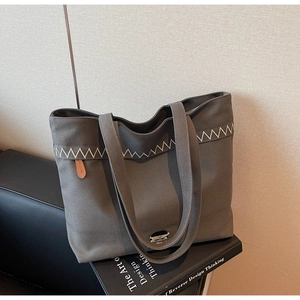 Detailed texture of charcoal grey canvas tote with white wavy embroidery on a sofa