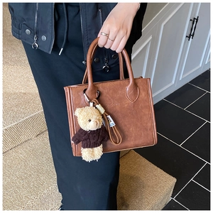 Detail of vintage brown leather square handbag with cute bear charm held on stairs