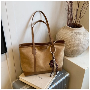 Macro detail of brown suede tote bag with leather trim and decorative bear charm