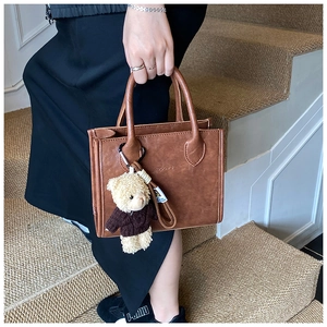 Detailed view of a vintage brown leather tote bag with a cute teddy bear charm on steps