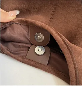 Close-up of silver magnetic clasp with geometric engraving on brown suede tote bag