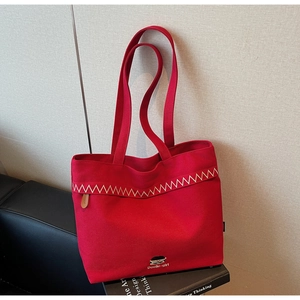 Detailed close-up of red canvas tote bag featuring golden wave stitching and logo