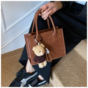 Detail of a brown leather tote bag with a small bear plush pendant on the handle strap