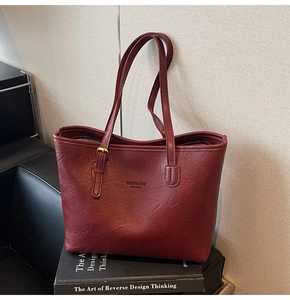 Detail of burgundy leather tote bag side view resting on a black art book