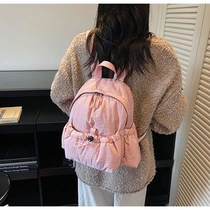 Detail view of pink nylon backpack featuring drawstring pocket and pleated fabric texture