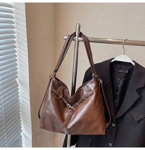Detail view of large dark brown leather tote bag with golden buckle on a metal hanger