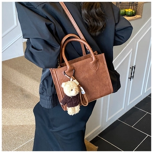 Detail of vintage brown leather tote bag with a cute bear pendant and top handles