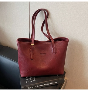 Close-up of burgundy tote bag with litchi texture and metal buckle on black books