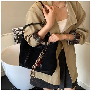 Detail of black suede tote bag with leather patchwork, gold logo, and tassel charm
