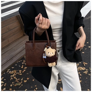Detailed texture of brown retro handbag with cute teddy bear charm in autumn outdoor setting