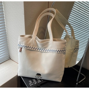 Detailed close-up of white canvas tote bag with blue wavy stitching and cartoon embroidery