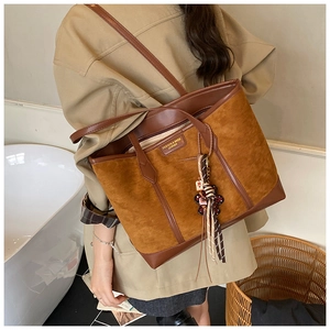 Brown vintage suede tote bag with decorative tassel and doll charm on a female model