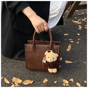 Detail of vintage dark brown square handbag with a cute teddy bear charm in autumn setting