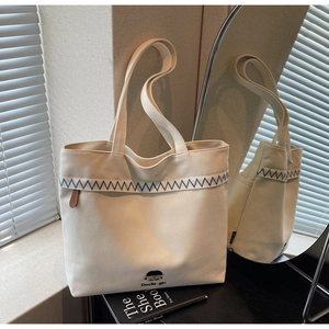 Close-up of beige canvas tote bag featuring blue zigzag embroidery and cartoon detail